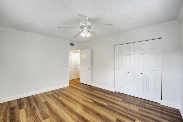 unfurnished bedroom with a closet, a textured ceiling, dark wood-type flooring, ornamental molding, and ceiling fan