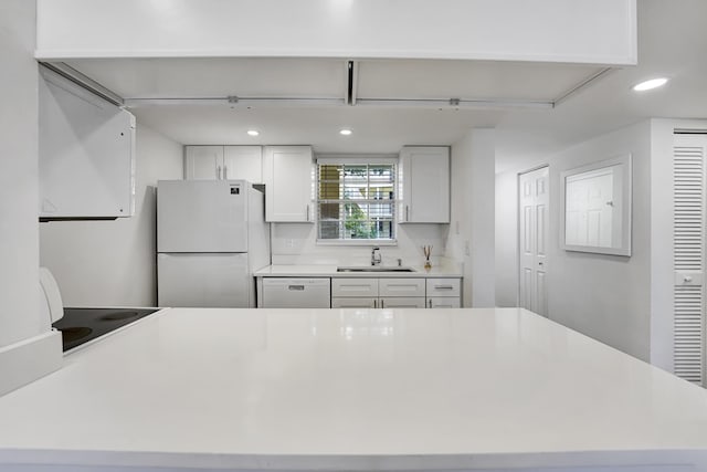 kitchen featuring a sink, light countertops, white appliances, white cabinetry, and recessed lighting