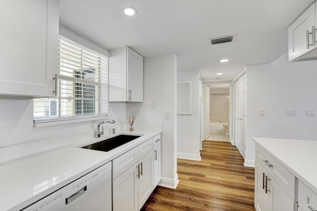 kitchen featuring white dishwasher, sink, hardwood / wood-style flooring, and white cabinetry