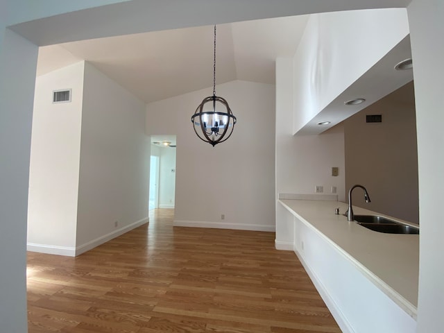 unfurnished dining area featuring vaulted ceiling, hardwood / wood-style flooring, sink, and a notable chandelier