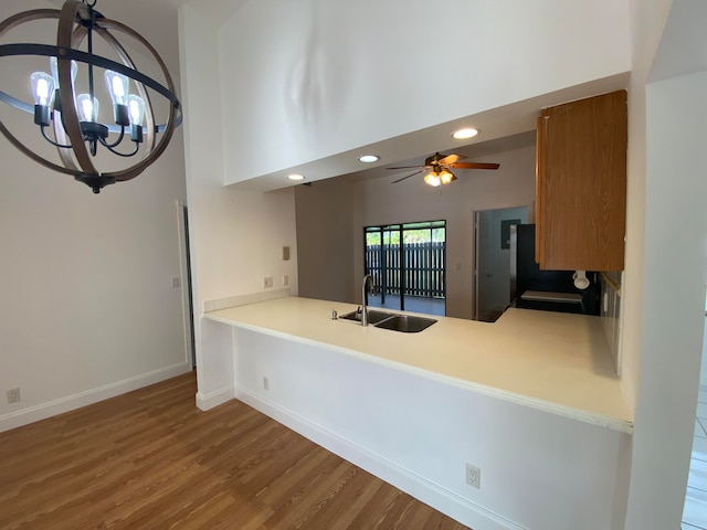 kitchen with hanging light fixtures, ceiling fan with notable chandelier, sink, wood-type flooring, and kitchen peninsula