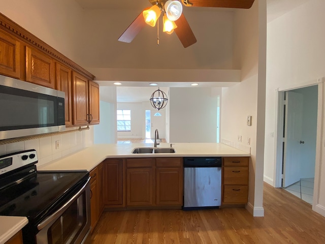 kitchen featuring stainless steel appliances, sink, ceiling fan with notable chandelier, and light hardwood / wood-style floors