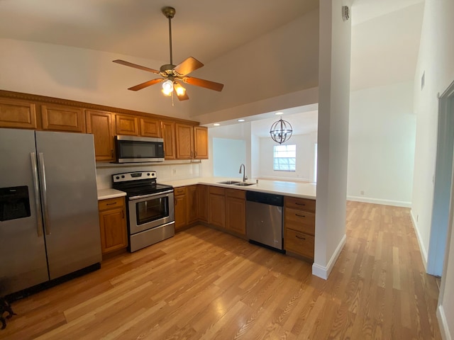 kitchen with ceiling fan with notable chandelier, light hardwood / wood-style flooring, appliances with stainless steel finishes, sink, and high vaulted ceiling