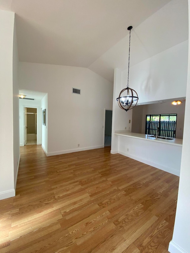 spare room with high vaulted ceiling, wood-type flooring, and an inviting chandelier