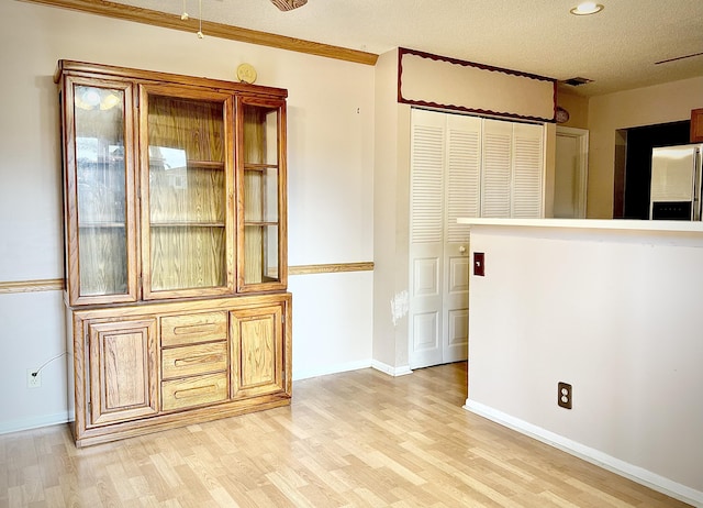 unfurnished dining area with a textured ceiling, crown molding, and light hardwood / wood-style floors