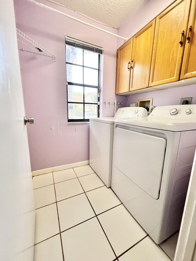 laundry room with a textured ceiling, cabinets, light tile patterned floors, and washing machine and clothes dryer