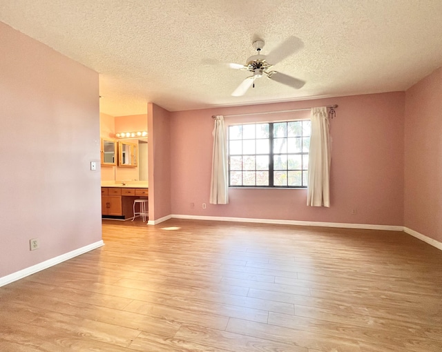 empty room with ceiling fan, a textured ceiling, built in desk, and light hardwood / wood-style floors