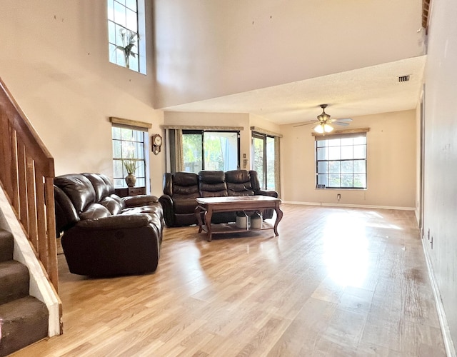 living room featuring ceiling fan, a high ceiling, and light hardwood / wood-style floors