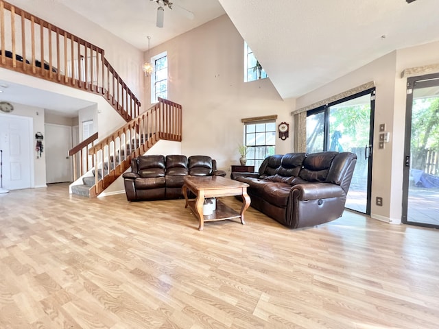 living room featuring a towering ceiling, ceiling fan with notable chandelier, and light hardwood / wood-style floors