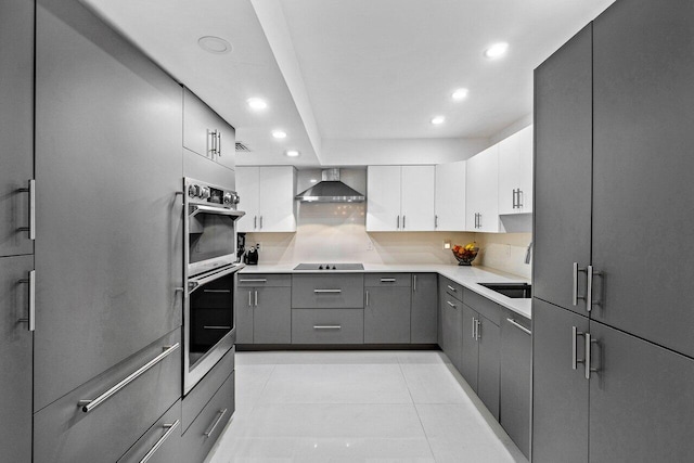 kitchen featuring white cabinets, light tile patterned flooring, tasteful backsplash, wall chimney range hood, and double oven