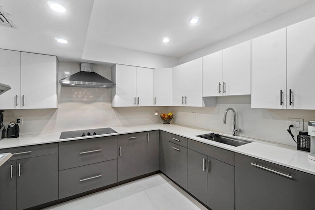 kitchen with black electric stovetop, sink, white cabinets, wall chimney exhaust hood, and backsplash