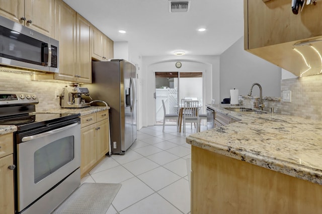 kitchen featuring appliances with stainless steel finishes, tasteful backsplash, sink, light brown cabinets, and light stone counters