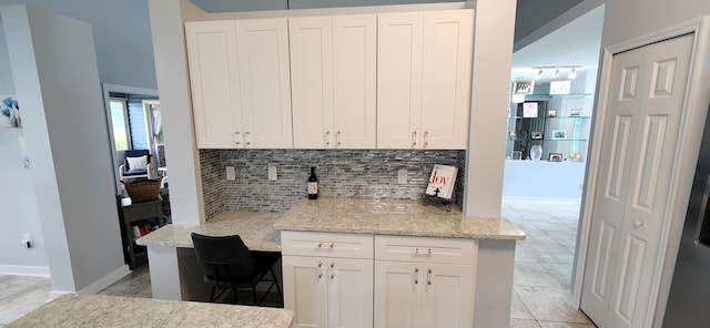 kitchen featuring light tile patterned flooring, light stone counters, white cabinets, and decorative backsplash