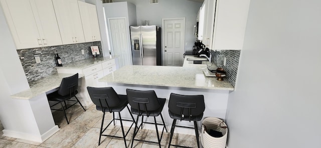 kitchen with stainless steel fridge with ice dispenser, a kitchen bar, kitchen peninsula, and white cabinets