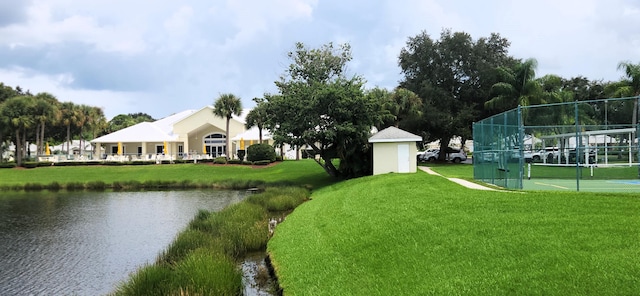 view of home's community with a water view, a lawn, and tennis court