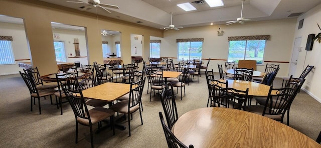 carpeted dining area featuring a raised ceiling, a skylight, and ceiling fan