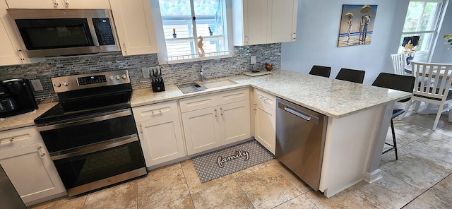 kitchen with stainless steel appliances, kitchen peninsula, white cabinets, and a breakfast bar area