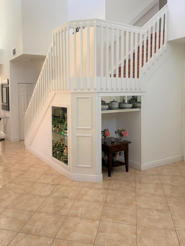 stairway with tile patterned floors, visible vents, baseboards, and a towering ceiling