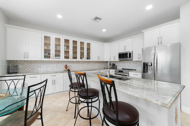 kitchen featuring visible vents, glass insert cabinets, light stone counters, appliances with stainless steel finishes, and white cabinets