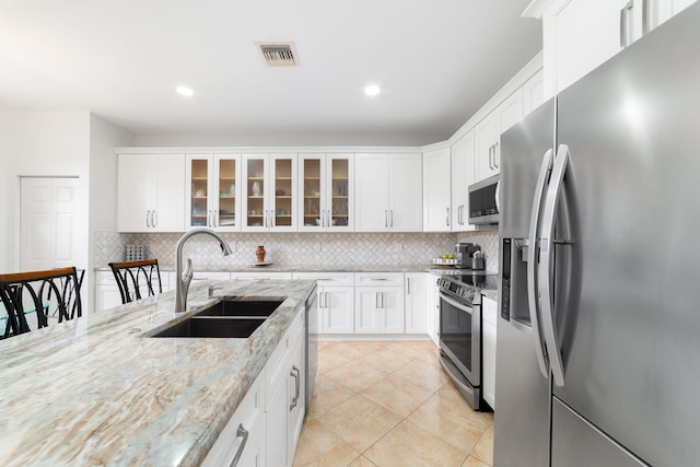 kitchen featuring visible vents, a sink, stainless steel appliances, white cabinets, and backsplash