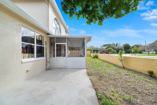 view of side of home featuring stucco siding, fence, and a sunroom