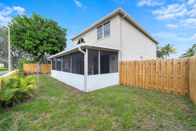 back of house featuring stucco siding, fence, a yard, and a sunroom