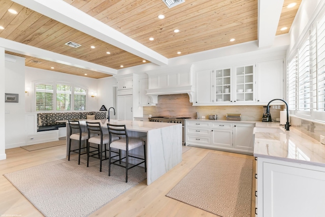 kitchen with white cabinetry, beam ceiling, decorative backsplash, light hardwood / wood-style flooring, and a center island with sink