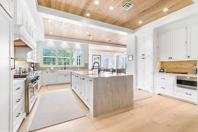 kitchen featuring an island with sink, white cabinetry, light wood-type flooring, appliances with stainless steel finishes, and tasteful backsplash