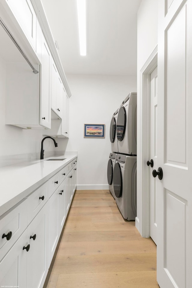 laundry room featuring cabinets, stacked washer and clothes dryer, sink, and light wood-type flooring