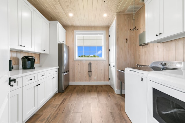 clothes washing area featuring wood walls, wood ceiling, washer and clothes dryer, hardwood / wood-style flooring, and cabinets