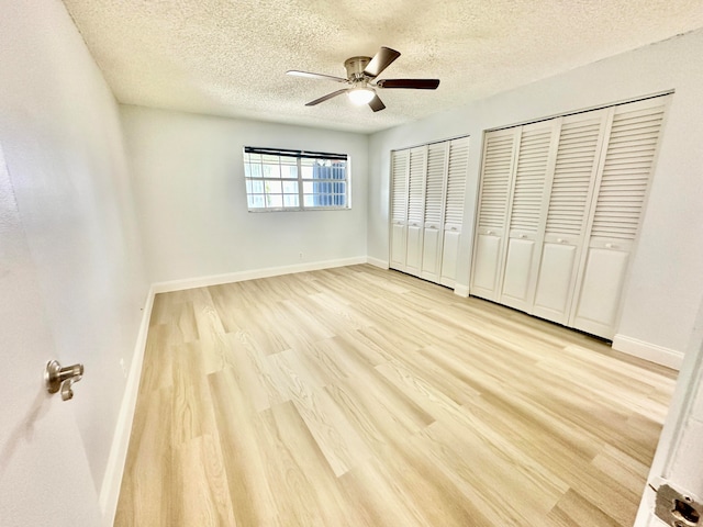 unfurnished bedroom with ceiling fan, a textured ceiling, light wood-type flooring, and two closets