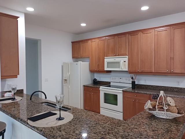 kitchen with kitchen peninsula, dark stone countertops, white appliances, and a kitchen breakfast bar