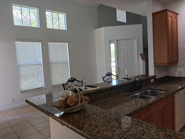 kitchen featuring dishwasher, sink, light tile patterned floors, and dark stone counters