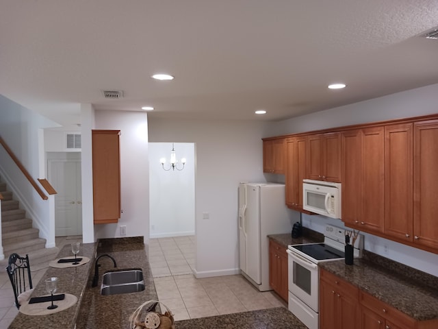 kitchen featuring dark stone countertops, white appliances, a notable chandelier, sink, and light tile patterned flooring