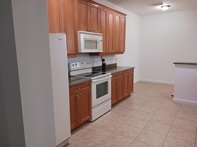 kitchen featuring dark stone countertops, light tile patterned floors, and white appliances