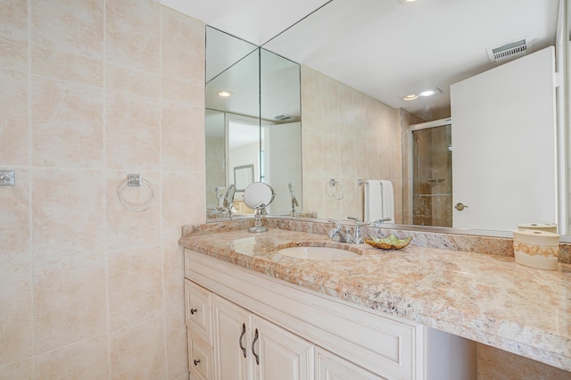 full bath featuring tile walls, vanity, visible vents, and a stall shower