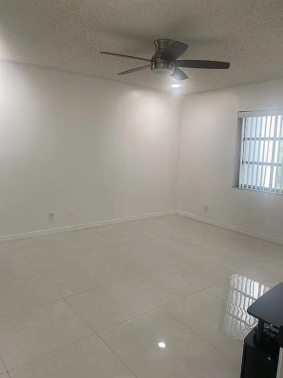 spare room featuring ceiling fan, light tile patterned floors, and a textured ceiling