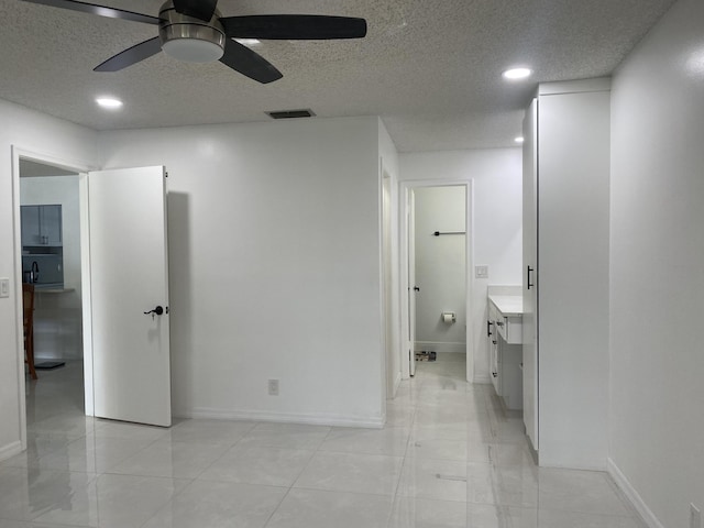 unfurnished bedroom with ceiling fan, a textured ceiling, and ensuite bath