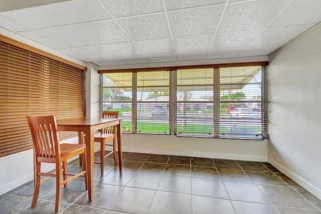 unfurnished dining area featuring a drop ceiling and dark tile patterned floors