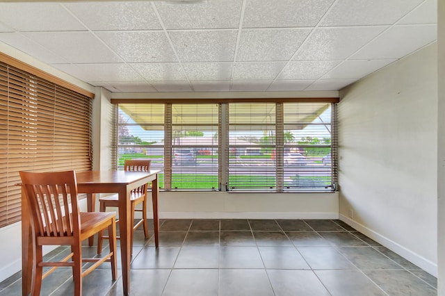 unfurnished dining area featuring a drop ceiling and dark tile patterned floors