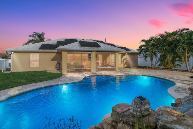 pool at dusk featuring a patio and a lawn