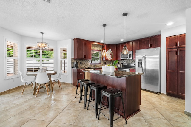 kitchen featuring backsplash, decorative light fixtures, a kitchen island, appliances with stainless steel finishes, and light tile patterned flooring