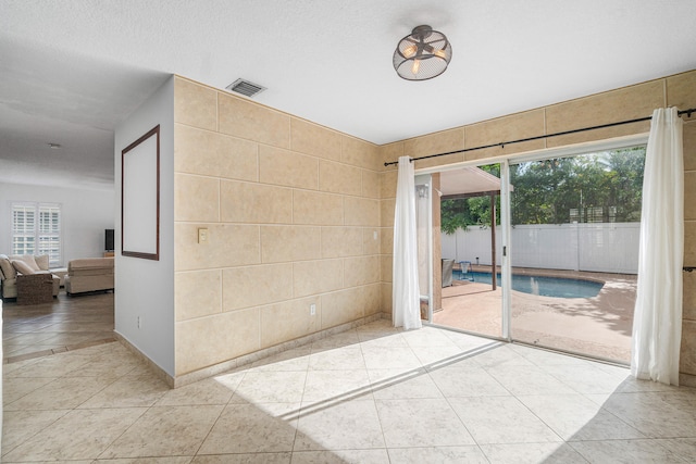 unfurnished room featuring tile walls, a wealth of natural light, light tile patterned flooring, and a textured ceiling