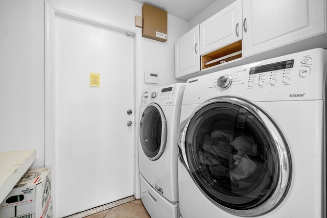 clothes washing area with separate washer and dryer, a textured ceiling, cabinets, and light tile patterned flooring