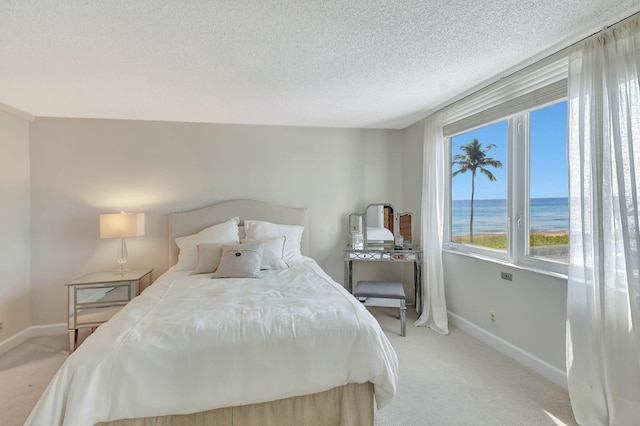 bedroom featuring a textured ceiling, a water view, and light carpet