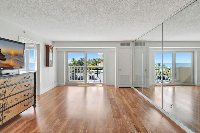 unfurnished living room with light wood-type flooring, a water view, and a textured ceiling