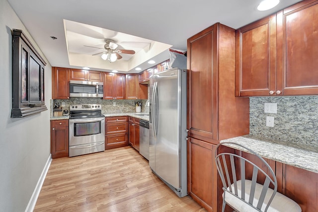 kitchen with tasteful backsplash, light hardwood / wood-style flooring, appliances with stainless steel finishes, light stone countertops, and ceiling fan