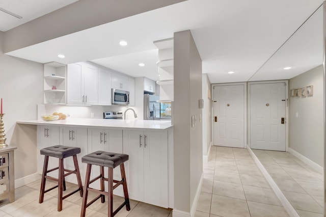 kitchen with white cabinets, stainless steel appliances, kitchen peninsula, a breakfast bar area, and light tile patterned flooring