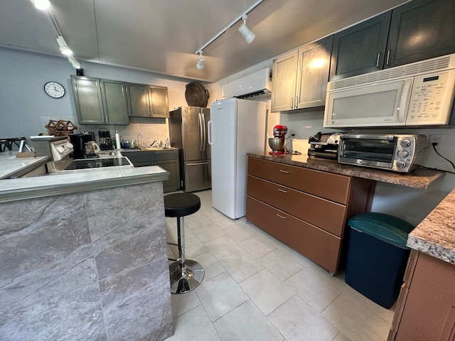 kitchen featuring track lighting, a wall mounted air conditioner, white appliances, a kitchen bar, and sink