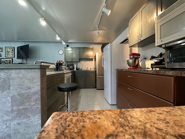 kitchen featuring track lighting, light tile patterned floors, stainless steel refrigerator, and sink